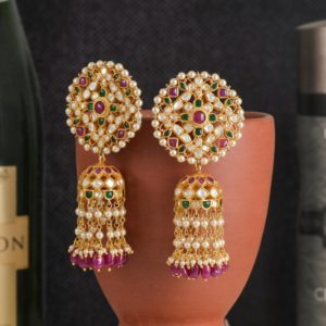 Exquisite gold earrings adorned with pearls and gemstones elegantly displayed on a clay pot.